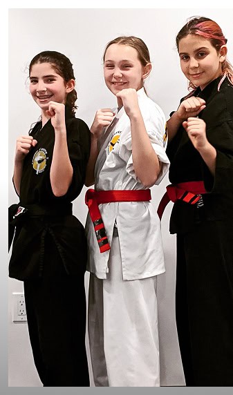 Three young martial arts students in uniform showing fighting stances at Johnny Karate NYC.
