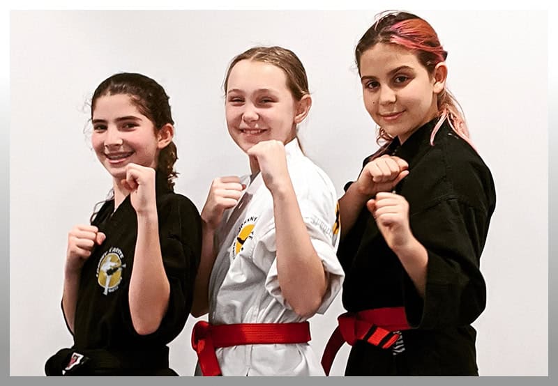 Three young girls in karate uniforms posing confidently in training gear.