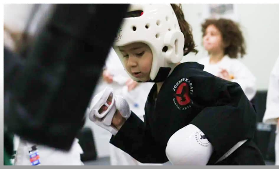 Young boy practicing martial arts in a preschool class with protective gear.