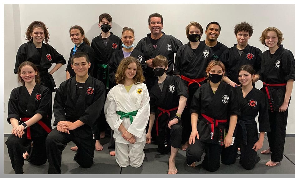 Group of teens in martial arts uniforms with instructor at Johnny Karate NYC dojo.