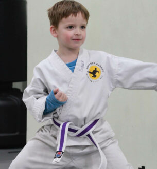 Young boy practicing karate in a white gi with purple belt at Johnny Karate NYC.