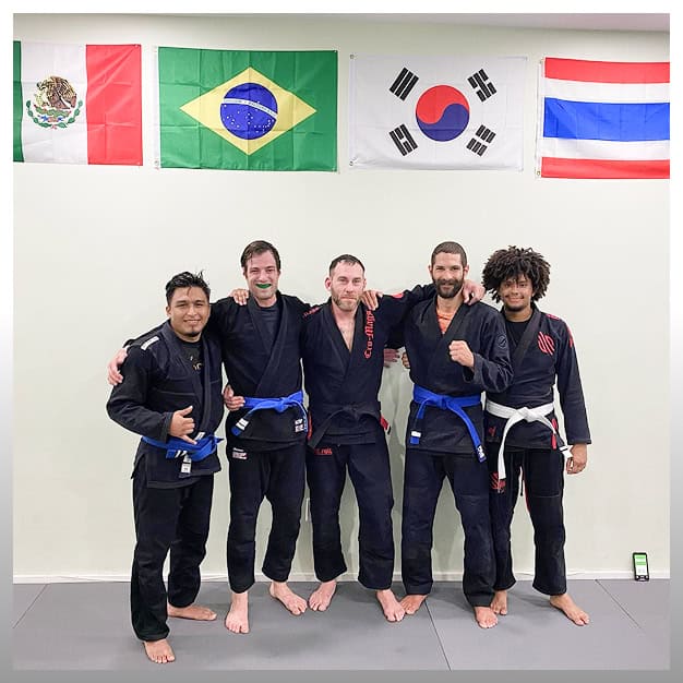 JMA Adult BJJ team practicing Brazilian Jiu-Jitsu in NYC with diverse flags background.