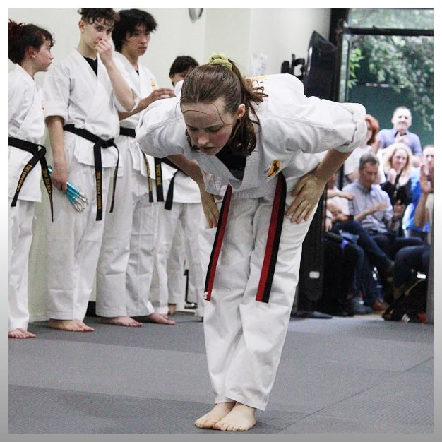 Teen girl bowing in martial arts class with peers in background.