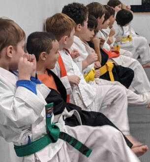 Kids martial arts class with young students in traditional uniforms sitting attentively.