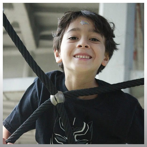 Child smiling during climbing activity at Johnny Karate NYC summer camp.