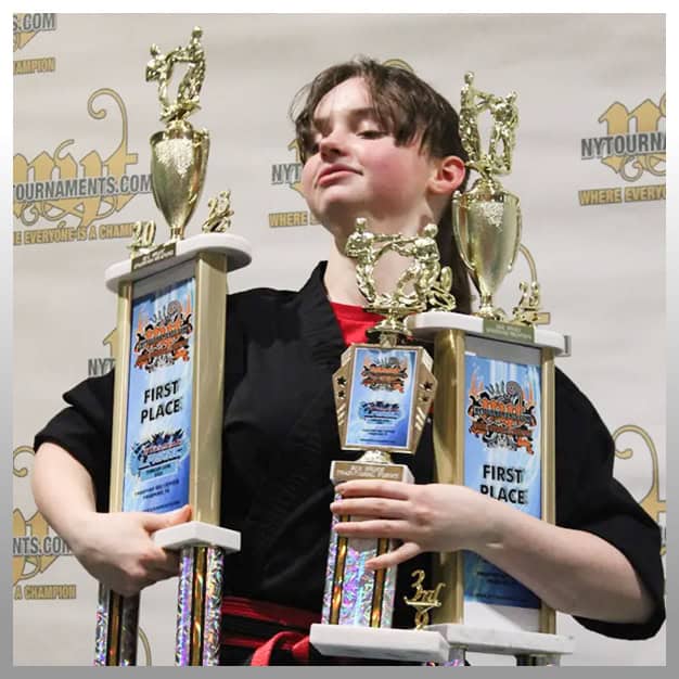Young boy with trophies celebrating martial arts victory at Teen Martial Arts event.